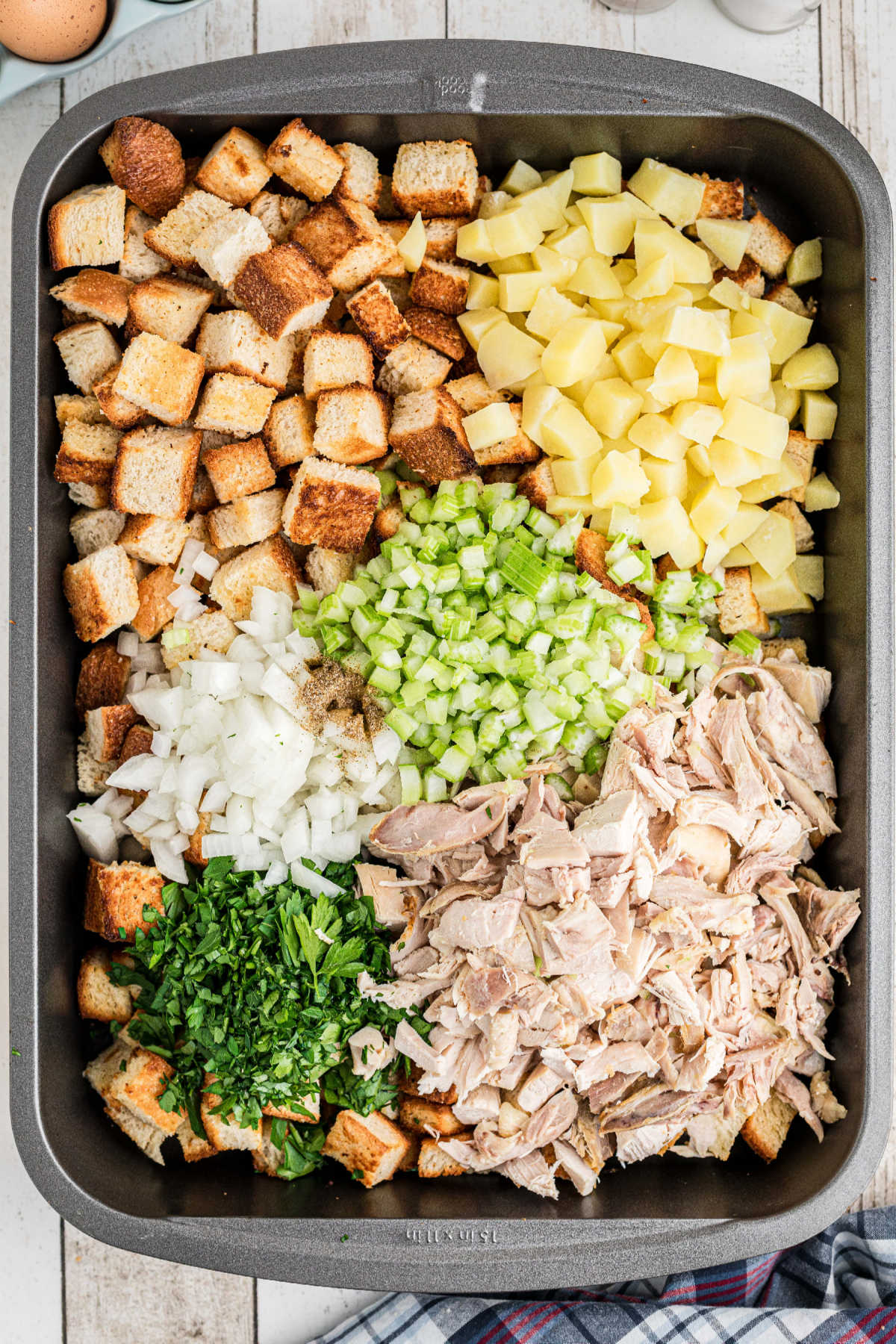 Cubes of bread, potatoes, turkey, onions, celery and seasonings added to a large roasting pan.