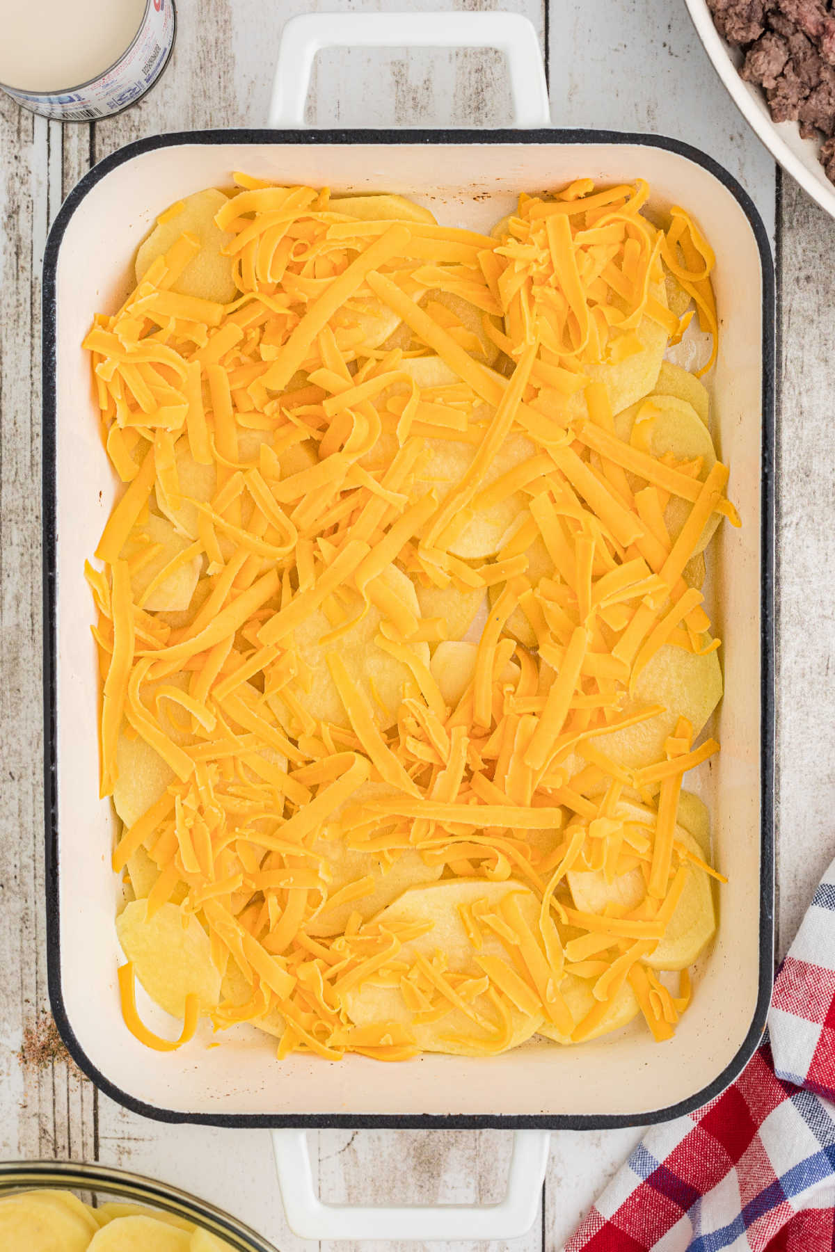 Cheese sprinkled on top of some potato slices in a baking dish.