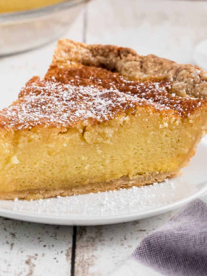 A slice of old fashioned chess pie with a dusting of powdered sugar, cropped square.