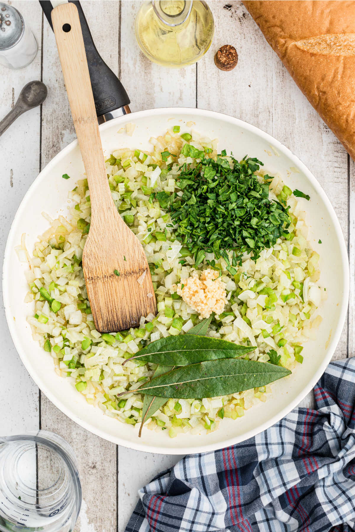 Bay leaves and garlic being added to a skillet full of veggies.