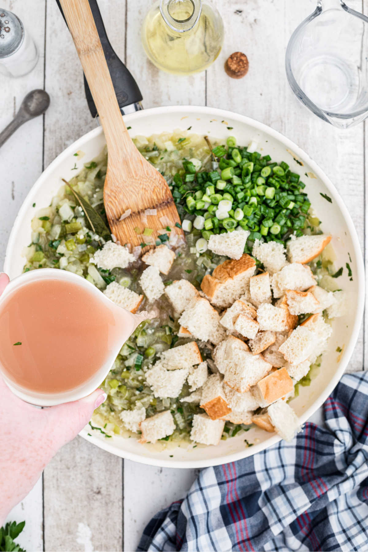 Bread cubes, onions and fresh oyster liquor being poured into the skillet.