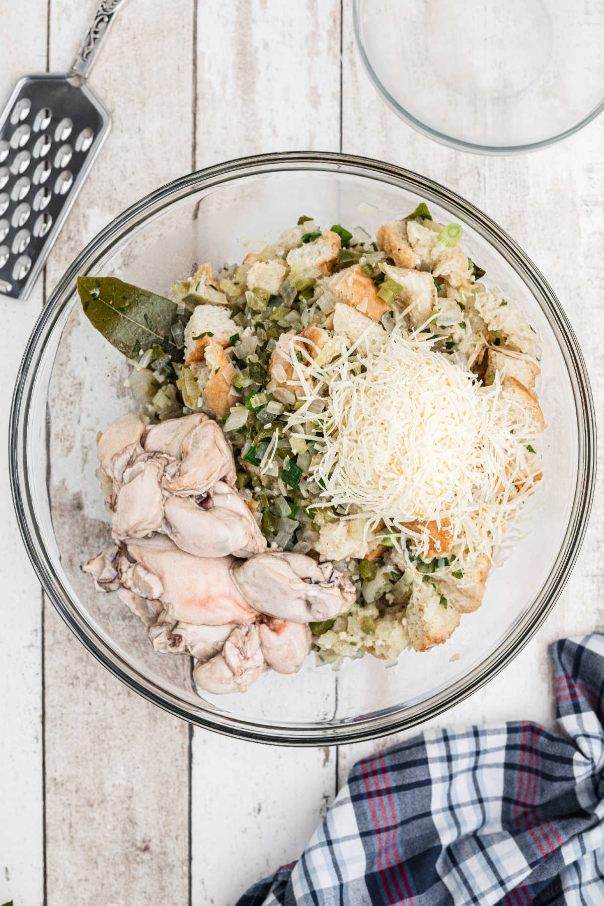 A large mixing bowl with cooked veggies, fresh oysters and parmesan cheese.