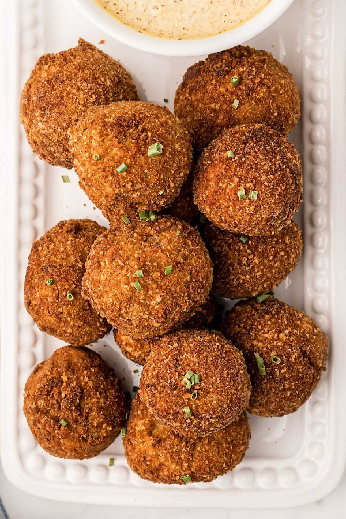 Boudin balls after having been fried, piled up on a plate with a dip.
