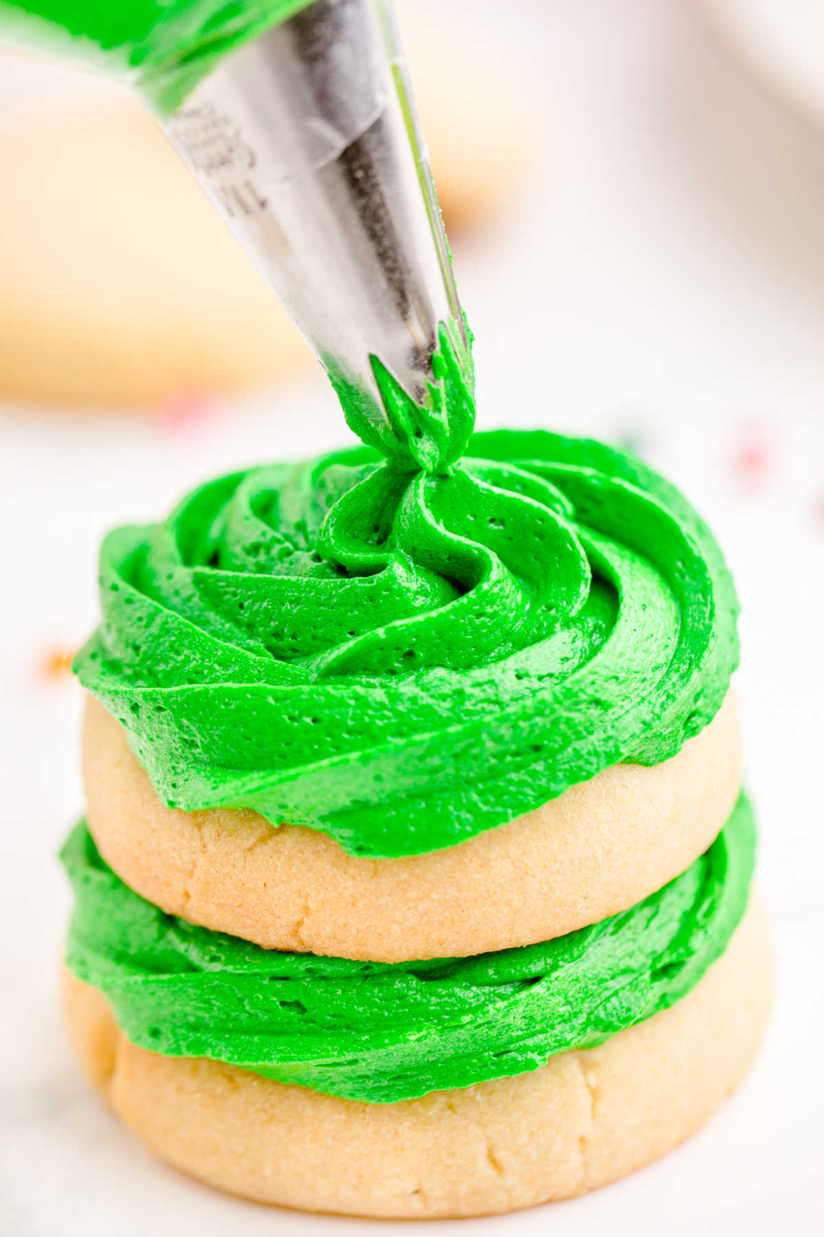 Frosting being piped onto sugar cookies in the shape of a Christmas tree.
