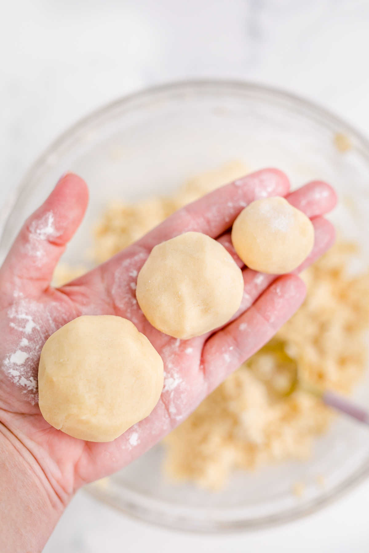 A hand with three different size cookie dough balls.