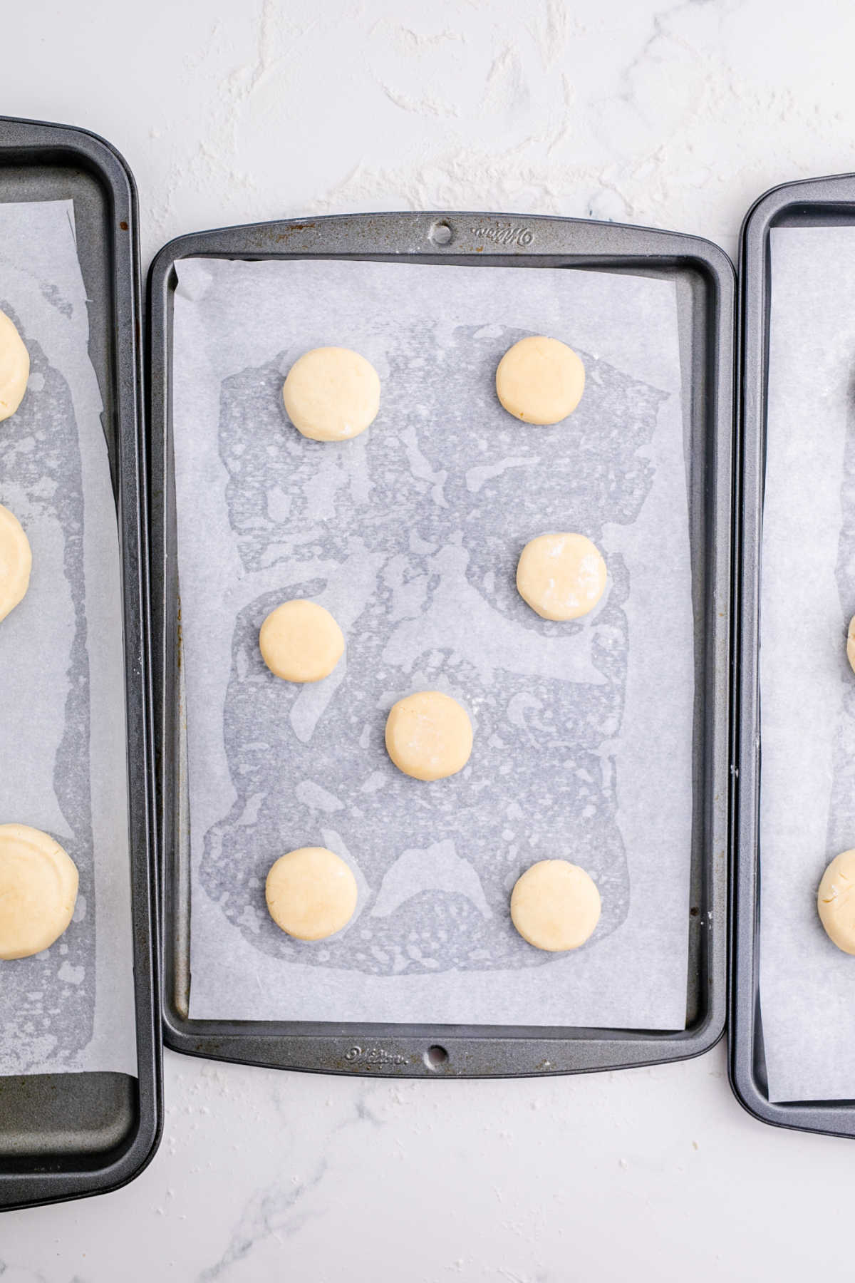 3 baking sheets with cookie dough balls waiting to be baked.