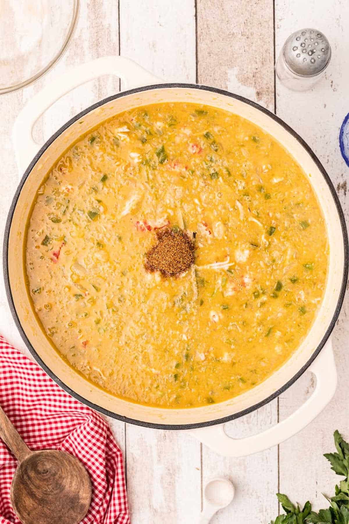 Seasoning added to a large Dutch oven filled with crawfish etouffee.