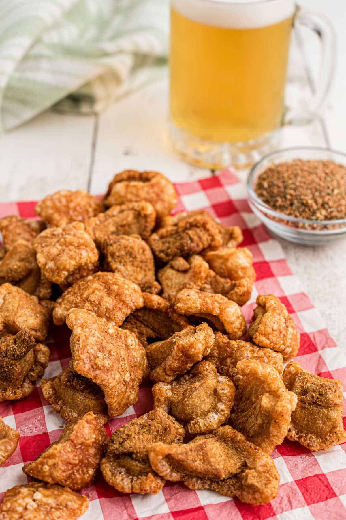 A pile of pork cracklins on a red napkin in front of a large beer.