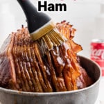 Close up of a basting brush glazing a southern coca-cola ham, with text overlay for pinterest.