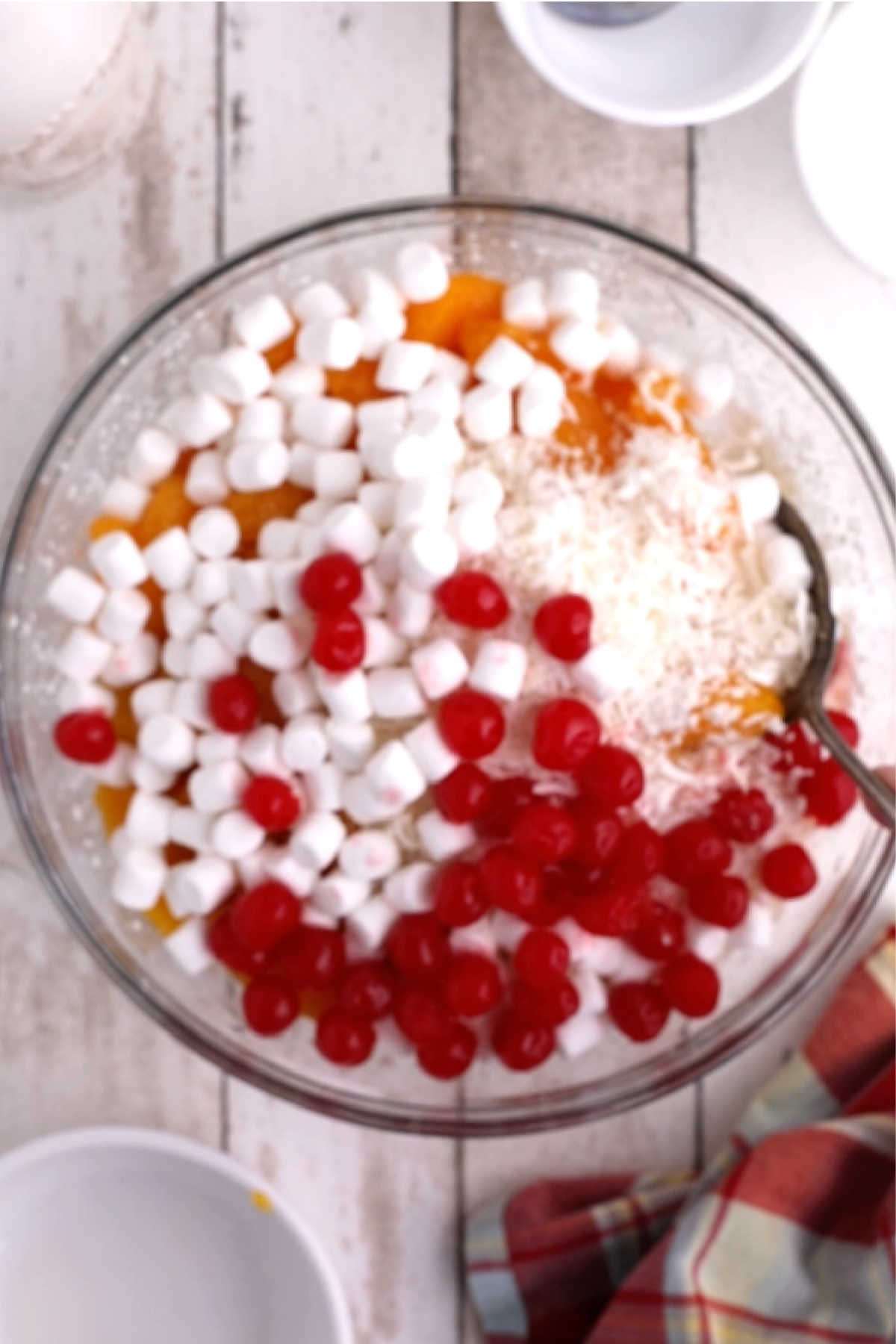 Cherries, marshmallows and coconut added to a bowl full of cream.