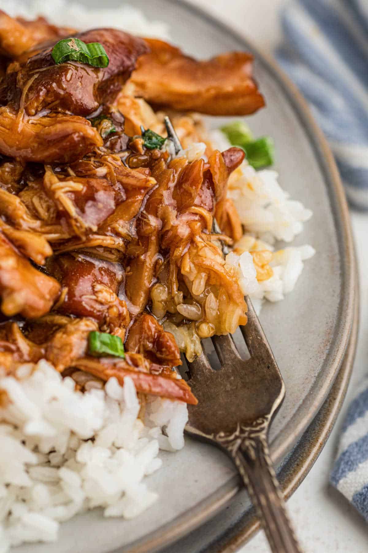 Really close up of a plate with bourbon chicken with rice and a fork digging in.
