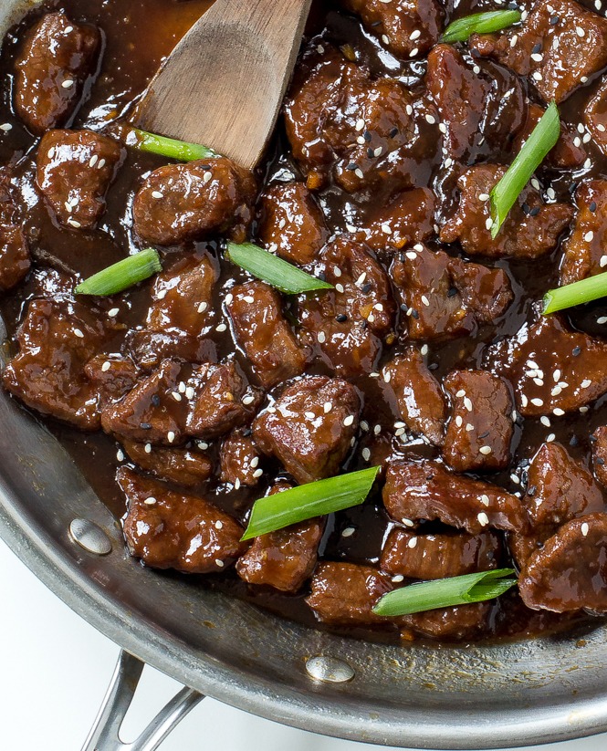 A skillet with some Chinese Mongolian Beef with green onions and sesame seeds sprinkled over.