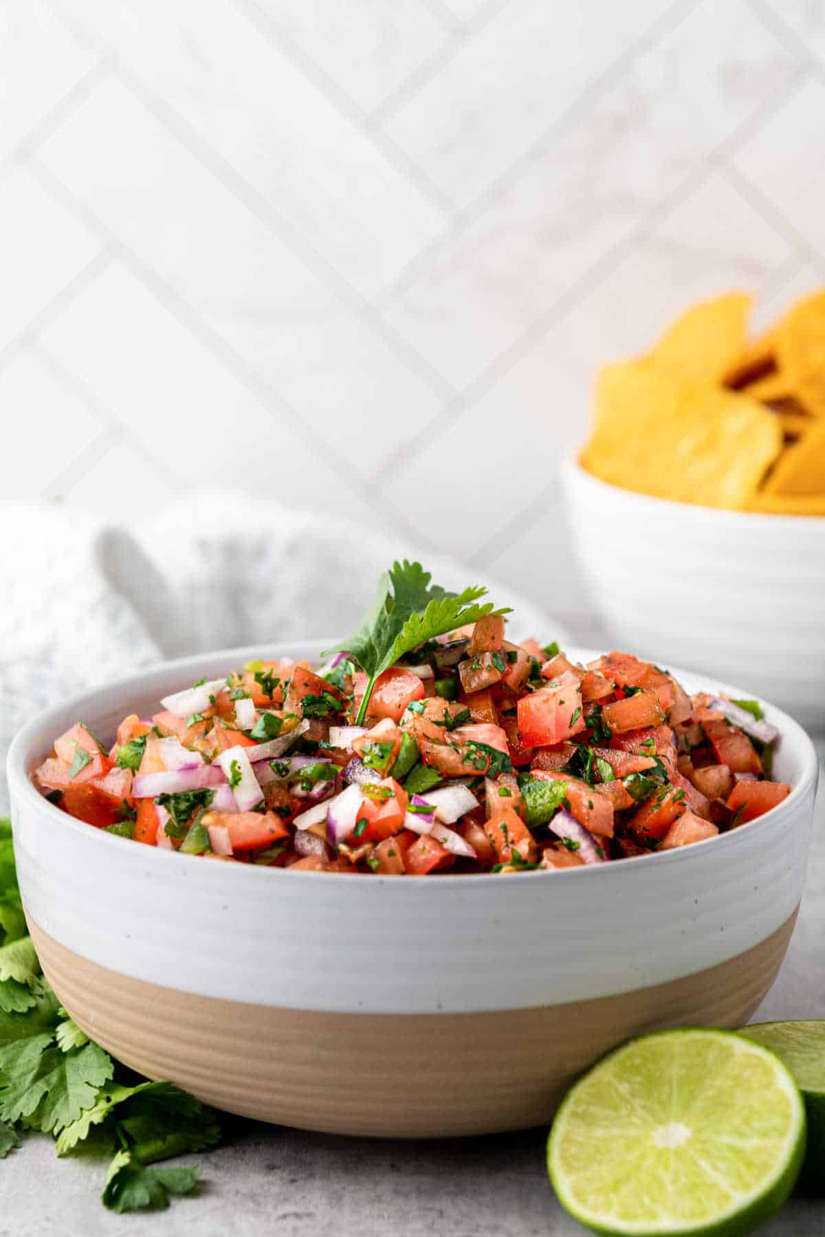 A side on view of a bowl of salsa fresca with some tortilla chips in the background.