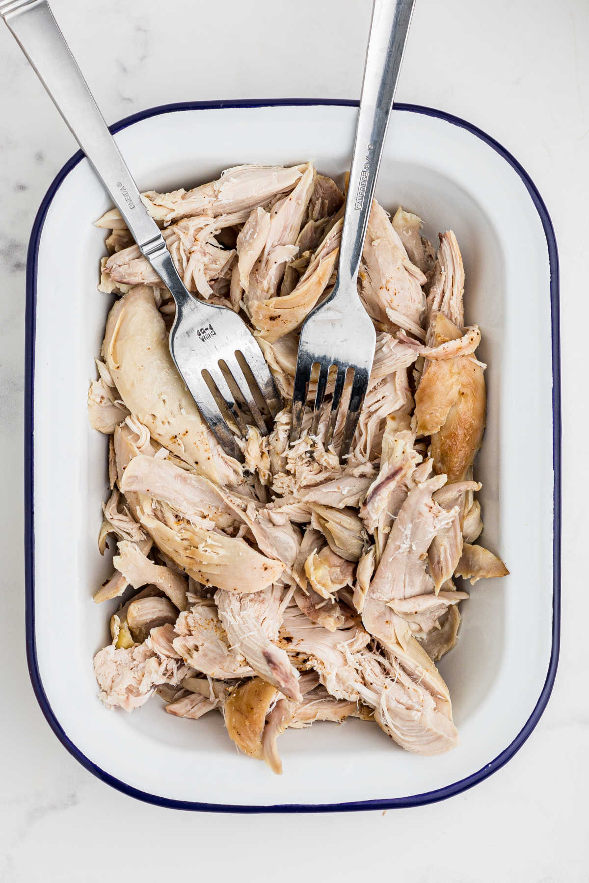 Cooked chicken in a dish with two forks shredding it.