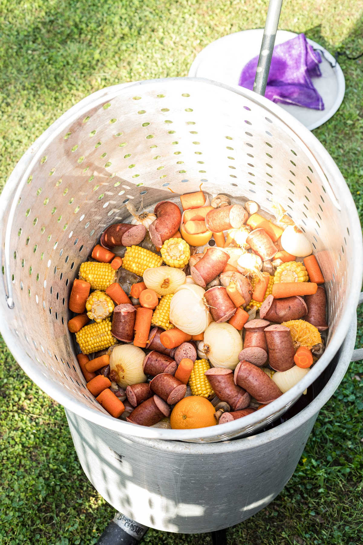A large boiling pot with basket filled with cooked vegetables and sausage.