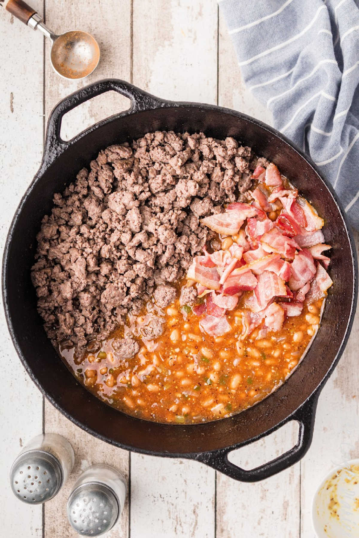 Ground beef and bacon added to a cast iron pot of beans.