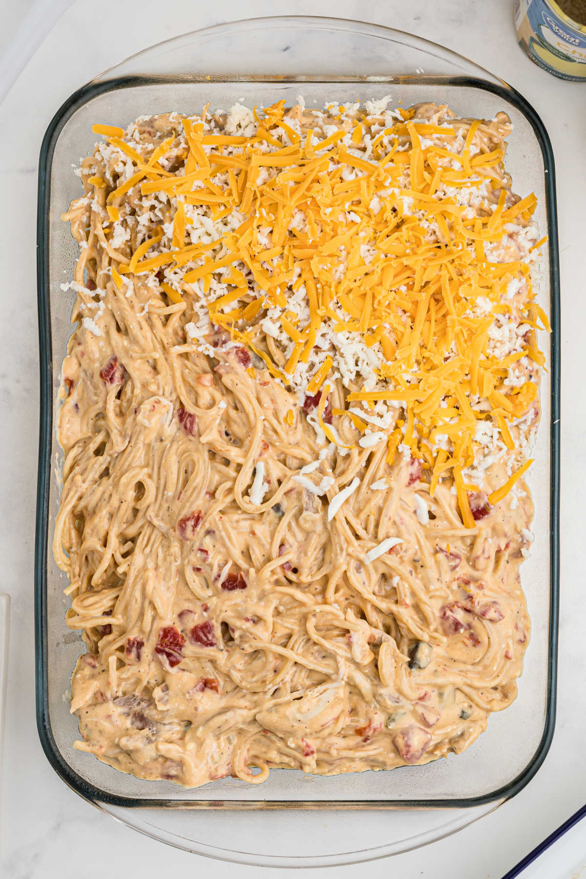 A large casserole dish with a chicken spaghetti filling, being topped with cheese.