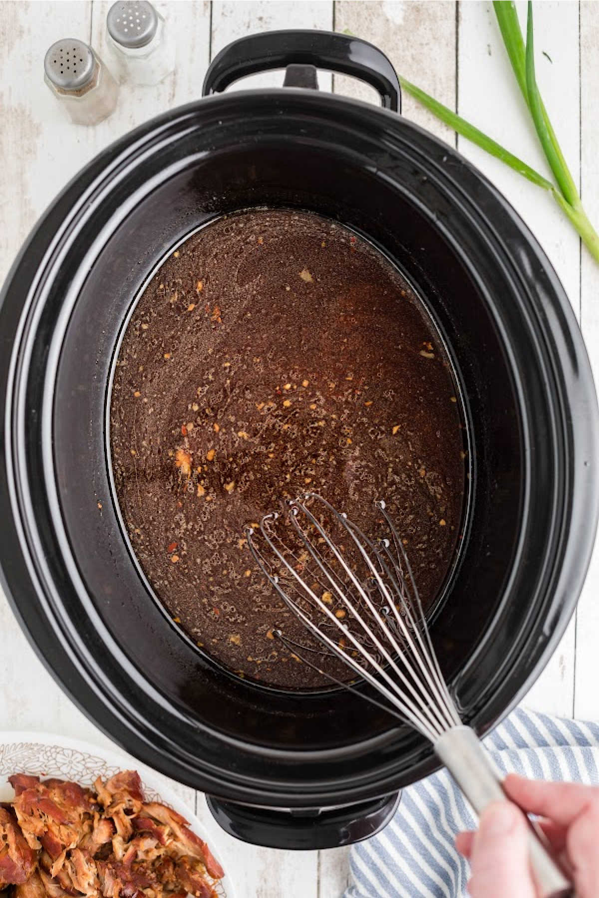 A crock pot with gravy and cornstarch being whisked together.