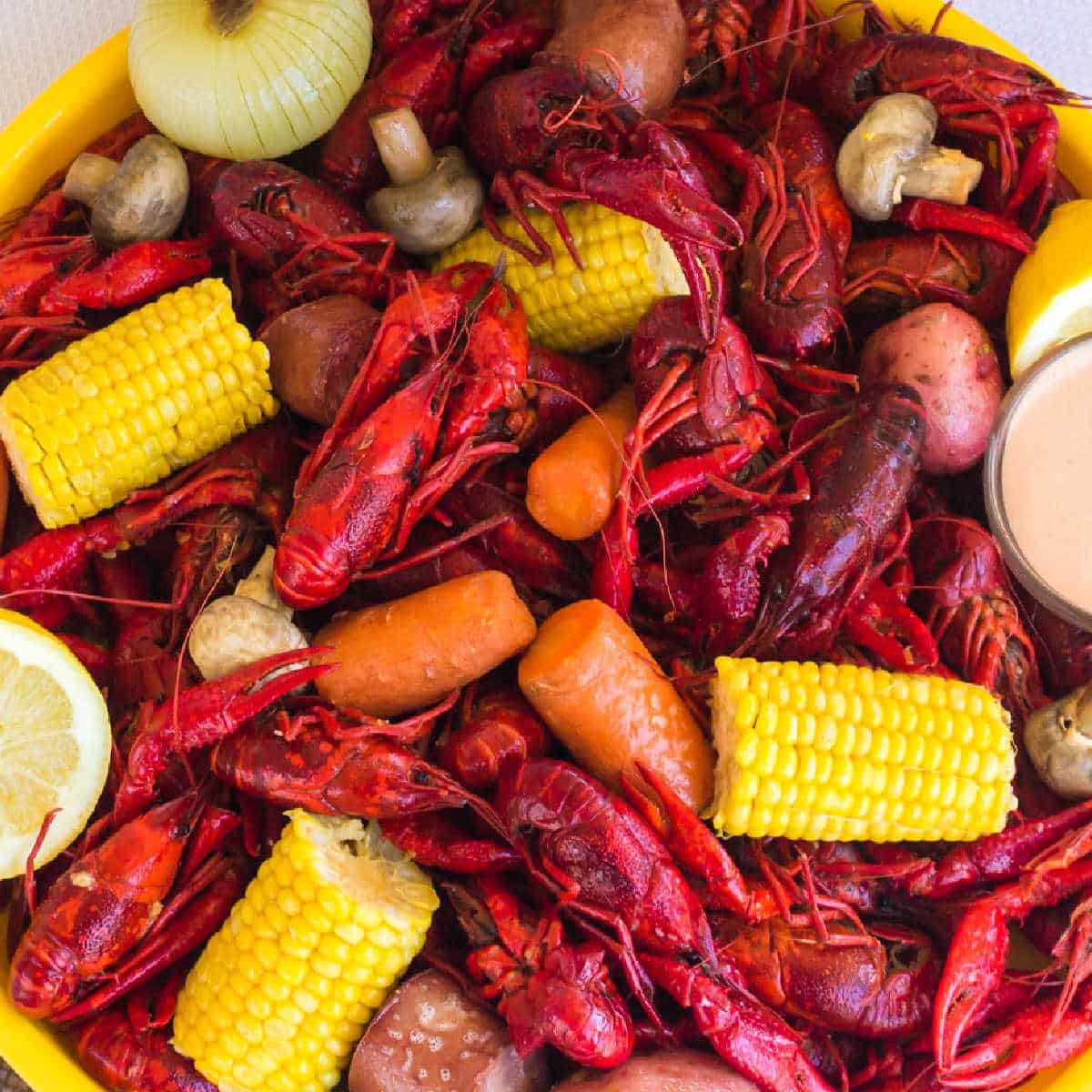 A large platter of boiled crawfish from a crawfish boil, with corn, sausage, potatoes, mushrooms and dip.