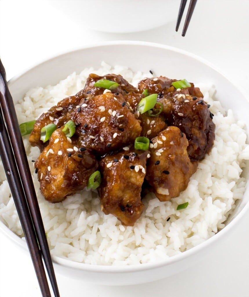 General Tso's Chicken made in the slow cooker. On a bed of rice, with chopsticks on the side.