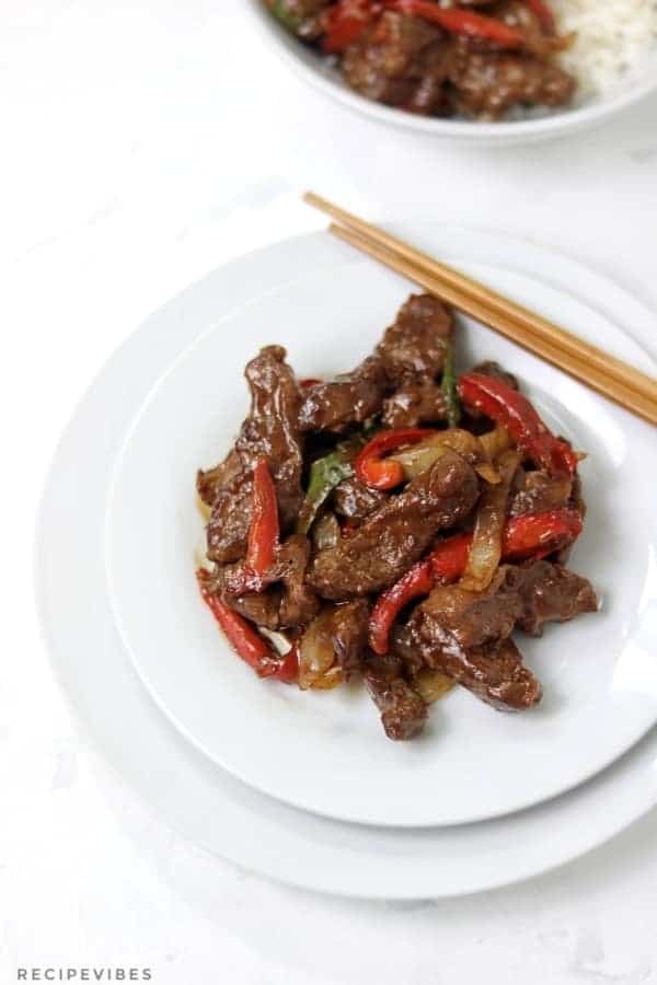 A single plate with some chinese pepper steak with peppers, and chopsticks resting on the side.