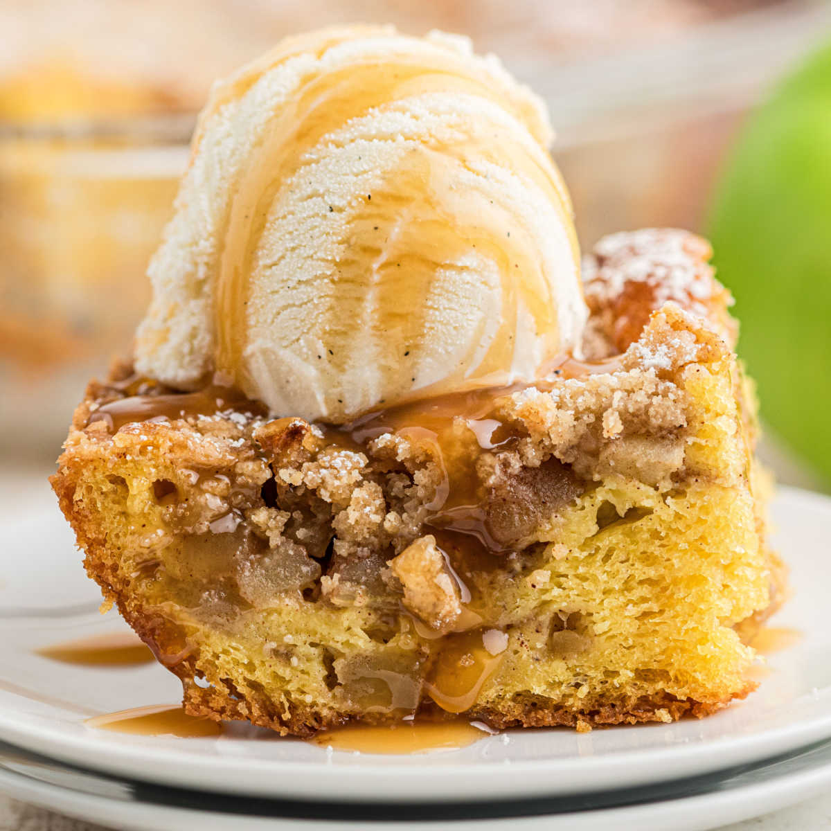Cropped square image, of a piece of apple pie cake with a scoop of ice cream on top.