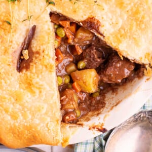 A square image of a beef pot pie, close up, with a slice missing.