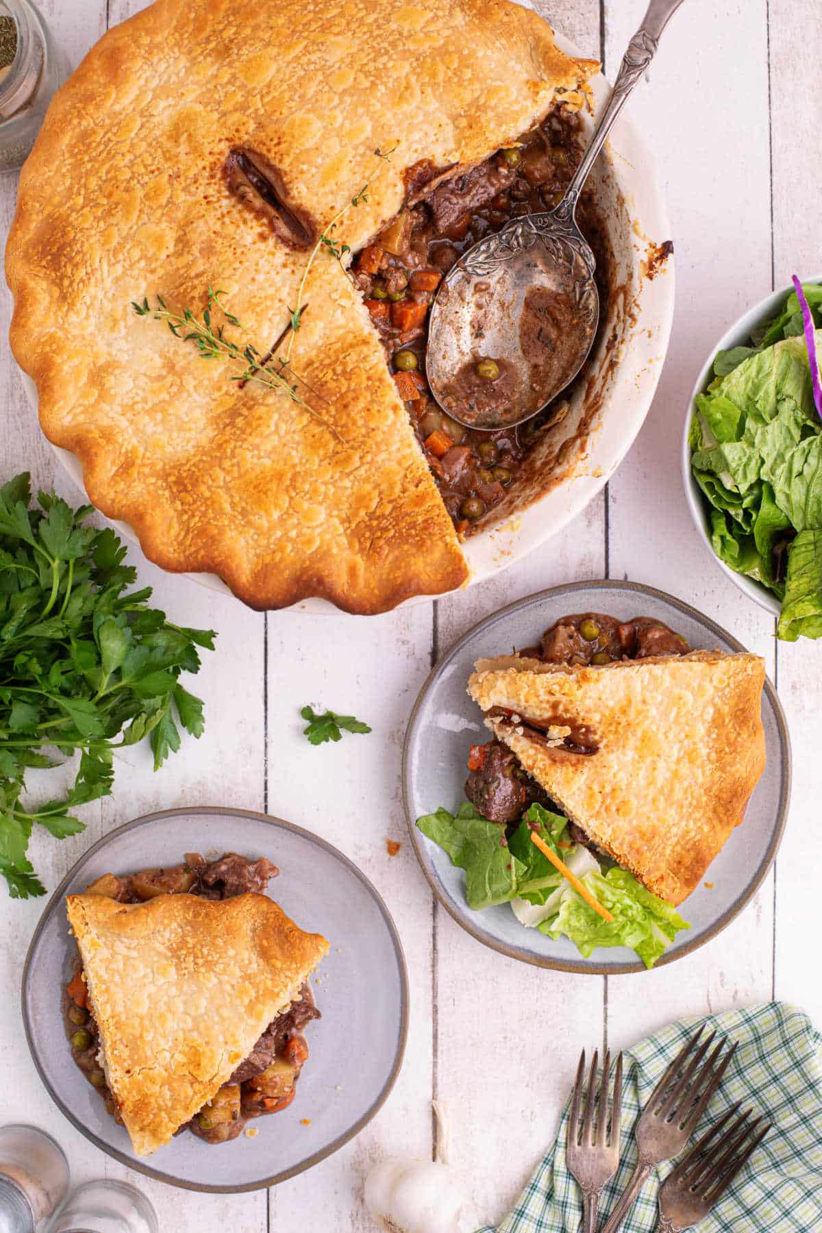 Overhead image of a beef pot pie with two slices on plates with some salad.
