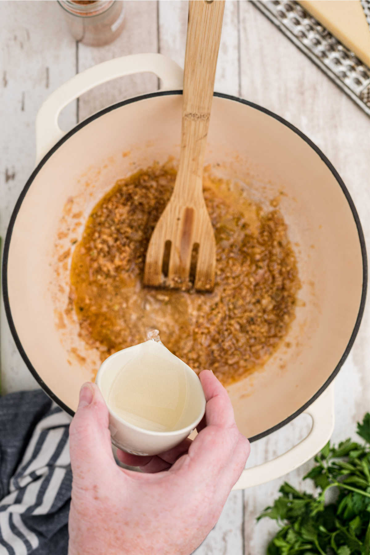 White wine being added to a pot with seasoned vegetables.