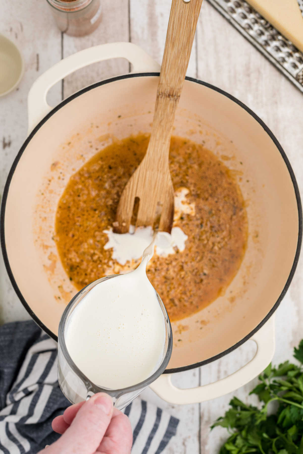 Cream being poured into a pot with shallots.