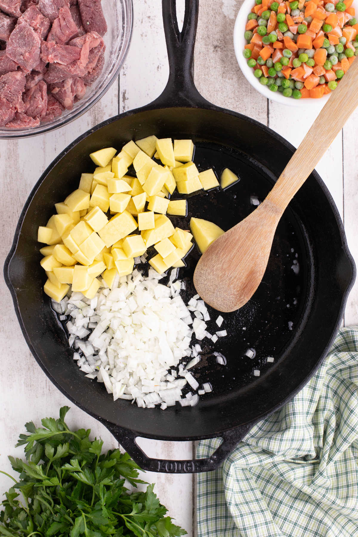 A large black skillet with oil, onions and potatoes in it.