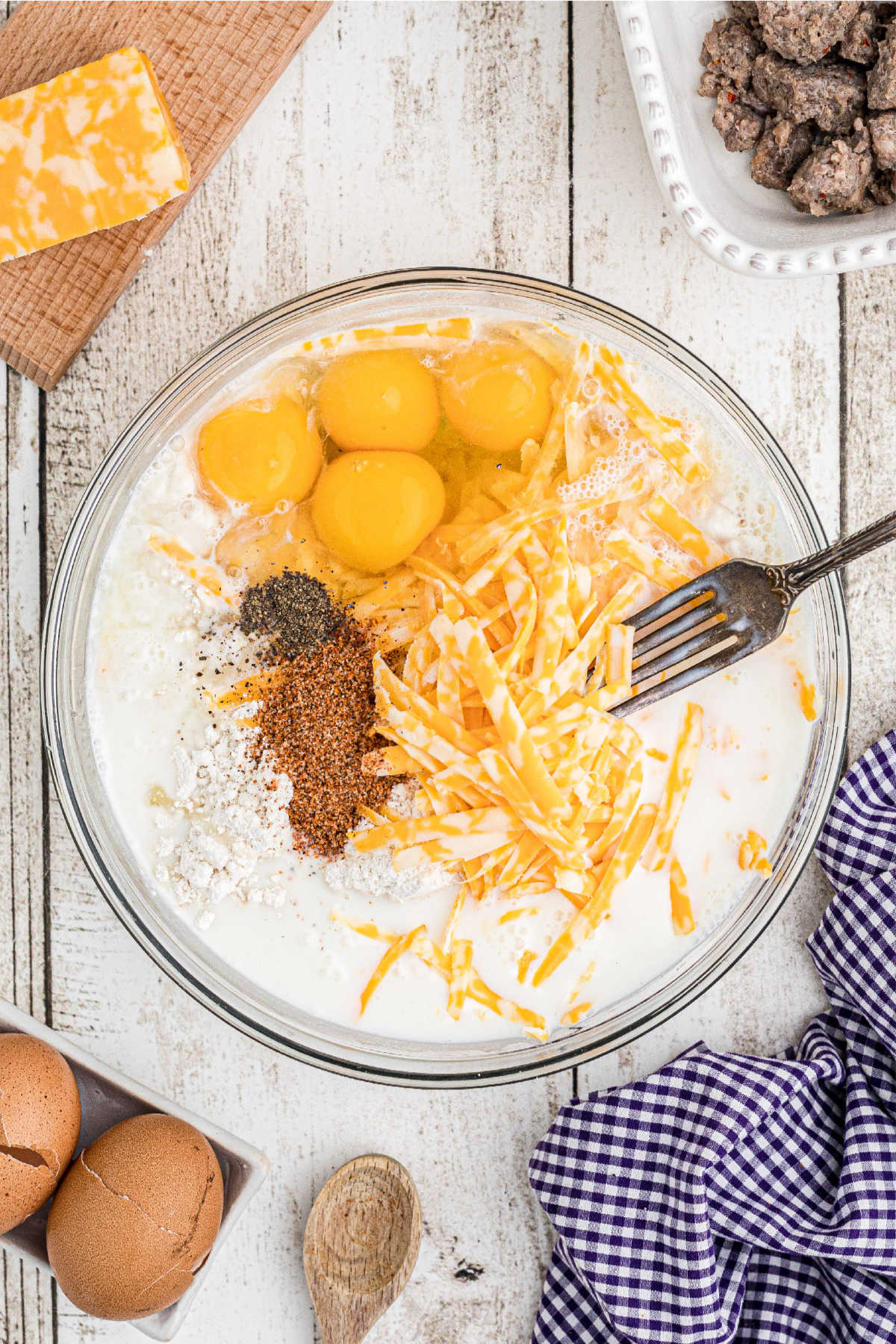 A large mixing bowl with eggs, cheese milk and seasonings.