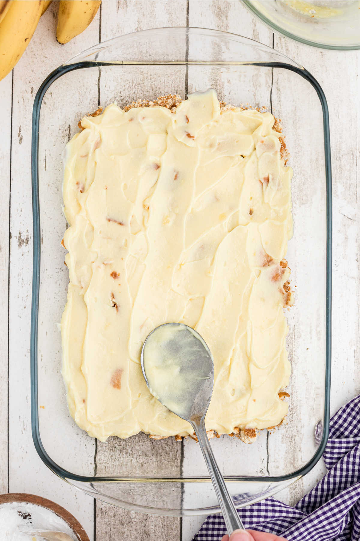 A baking dish with pudding being spread on top of crushed cookies.