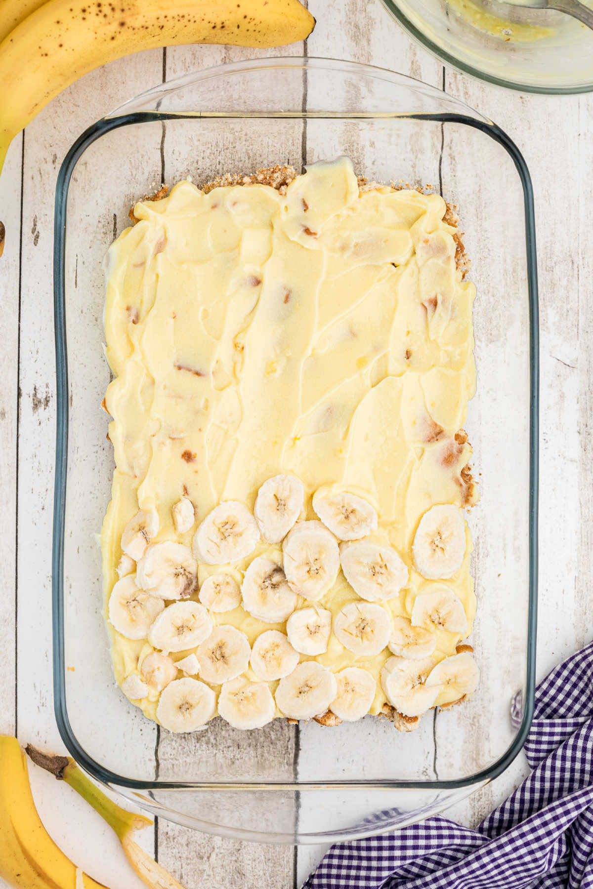 Sliced bananas being laid on top of pudding in a baking dish.