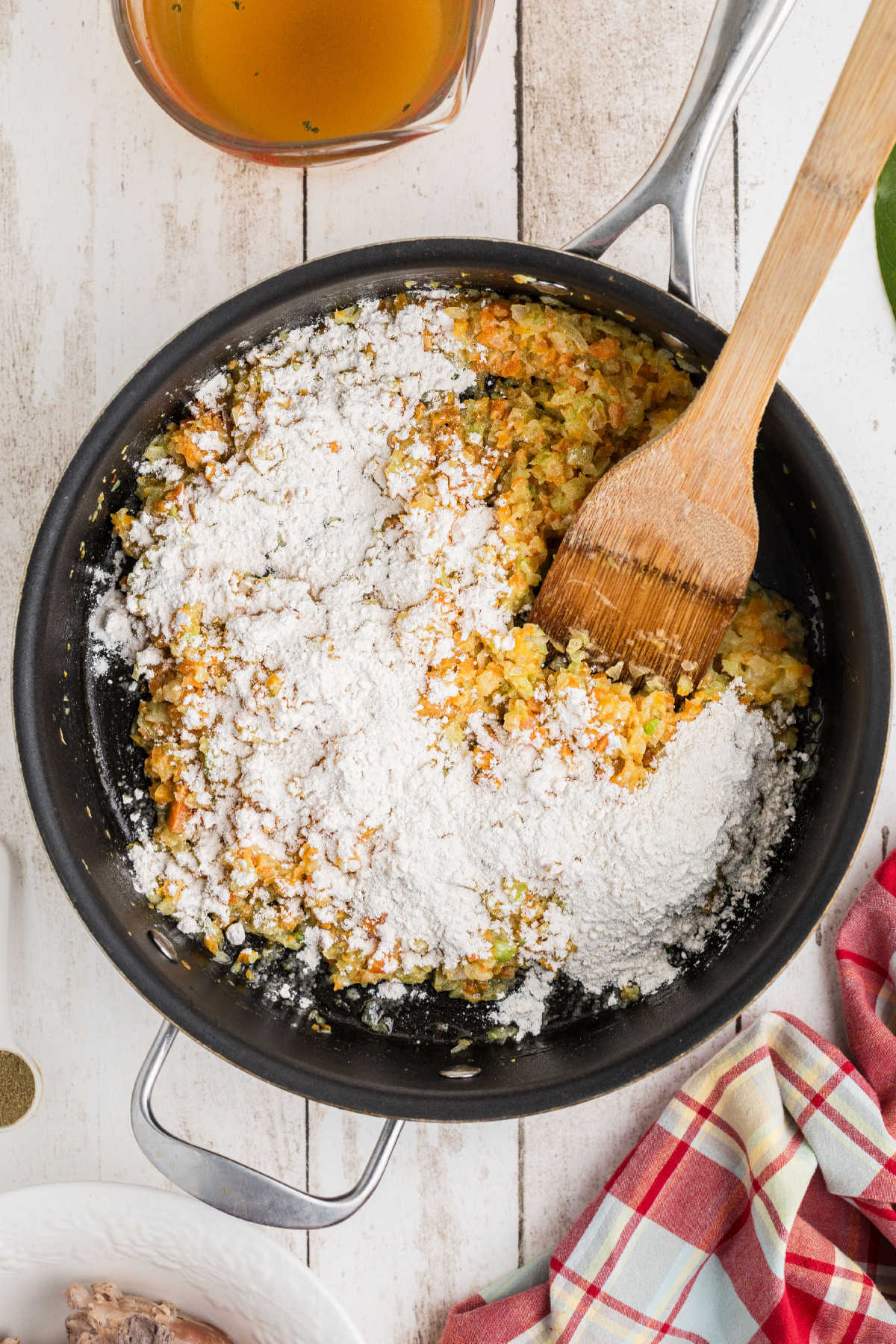 Flour added to a skillet of cooking vegetables.