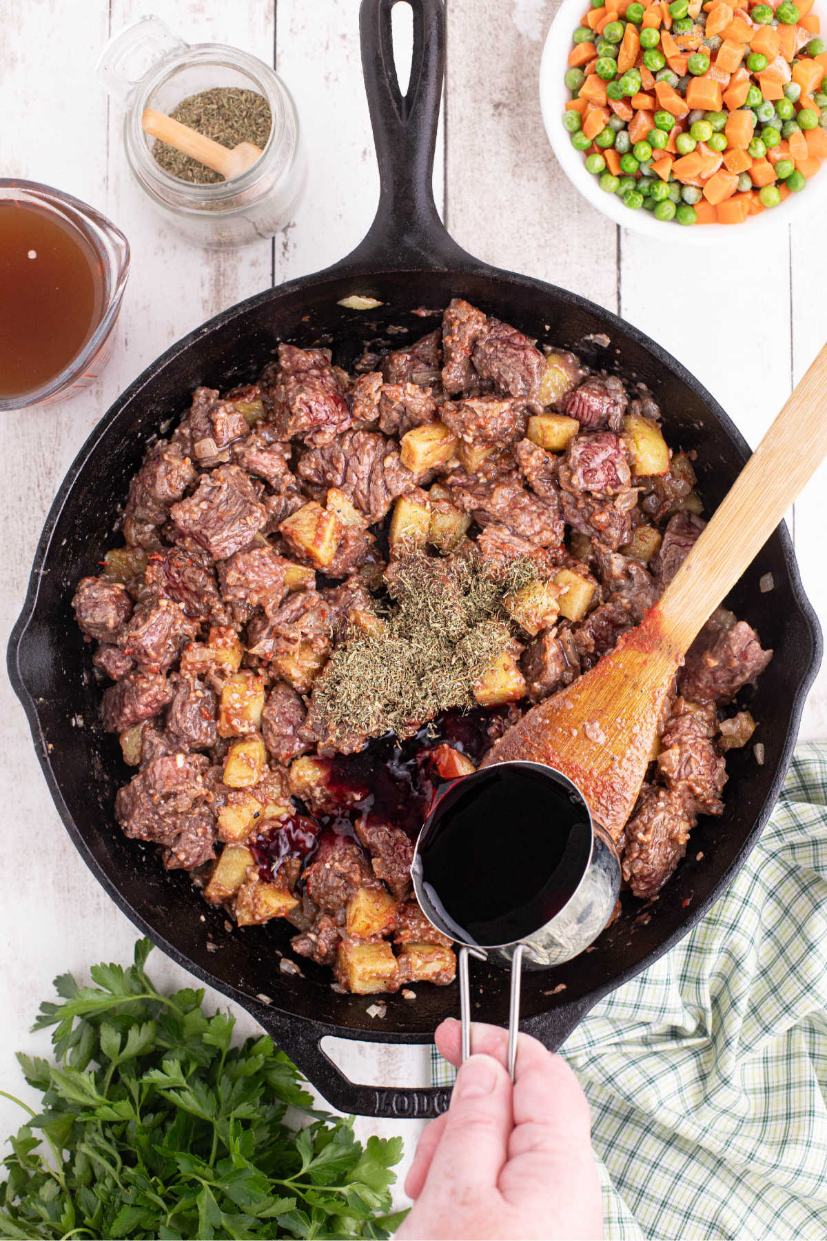 Beef and potatoes cooking in a large black skillet with red wine being poured in.
