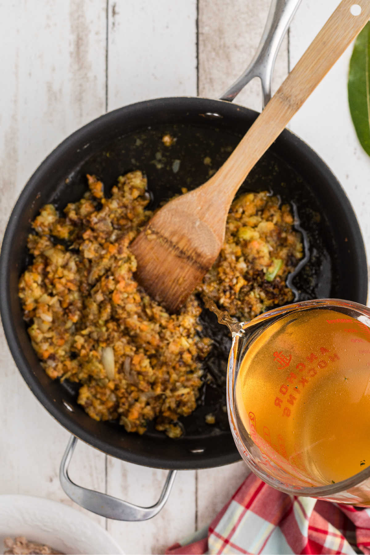 Slowly pouring chicken broth into a large skillet of cooking vegetables.