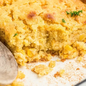Close up shot of a dish of cornbread pudding with a wooden spoon resting.