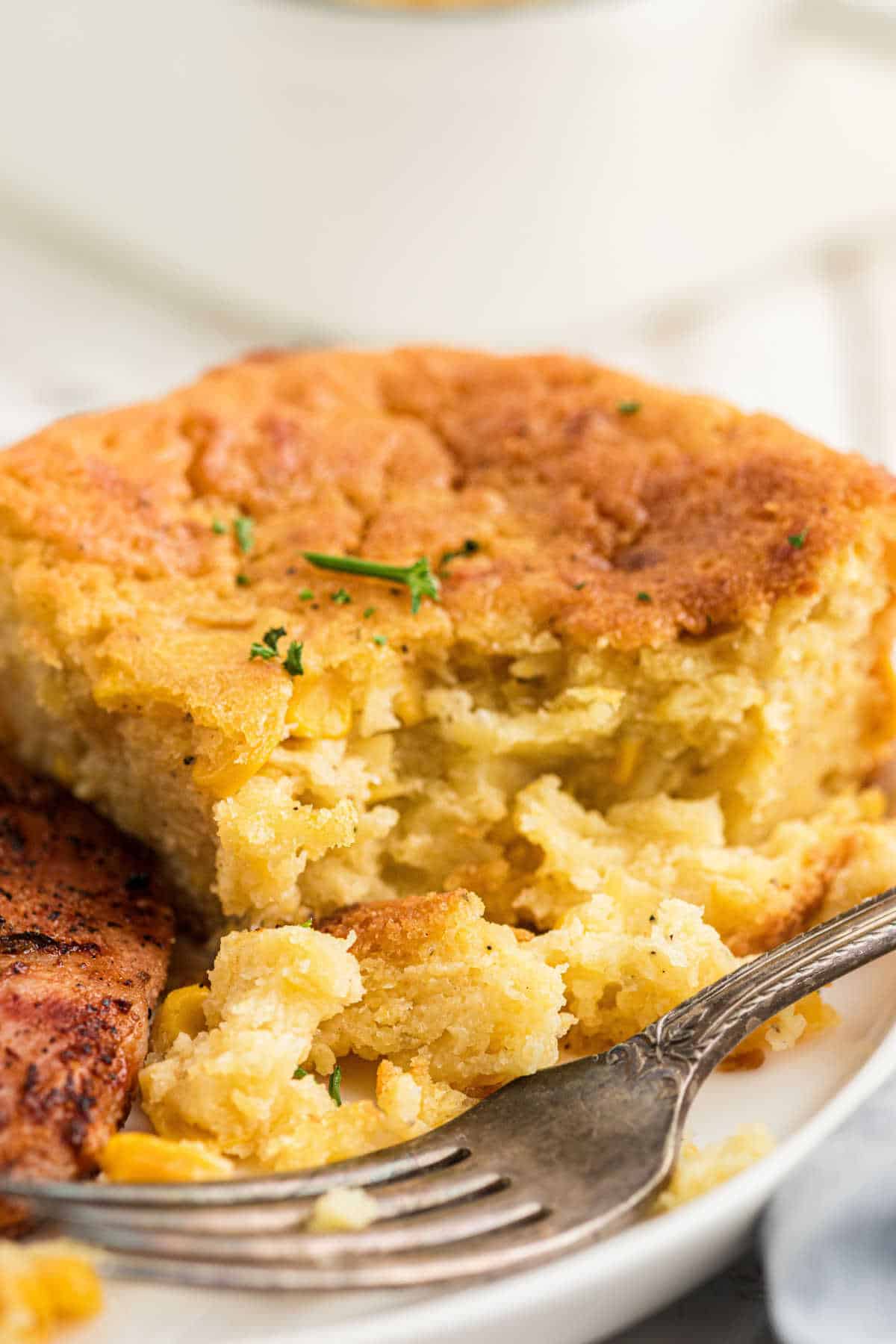 Close up of a dished up serving of cornbread pudding with a fork resting next to it.