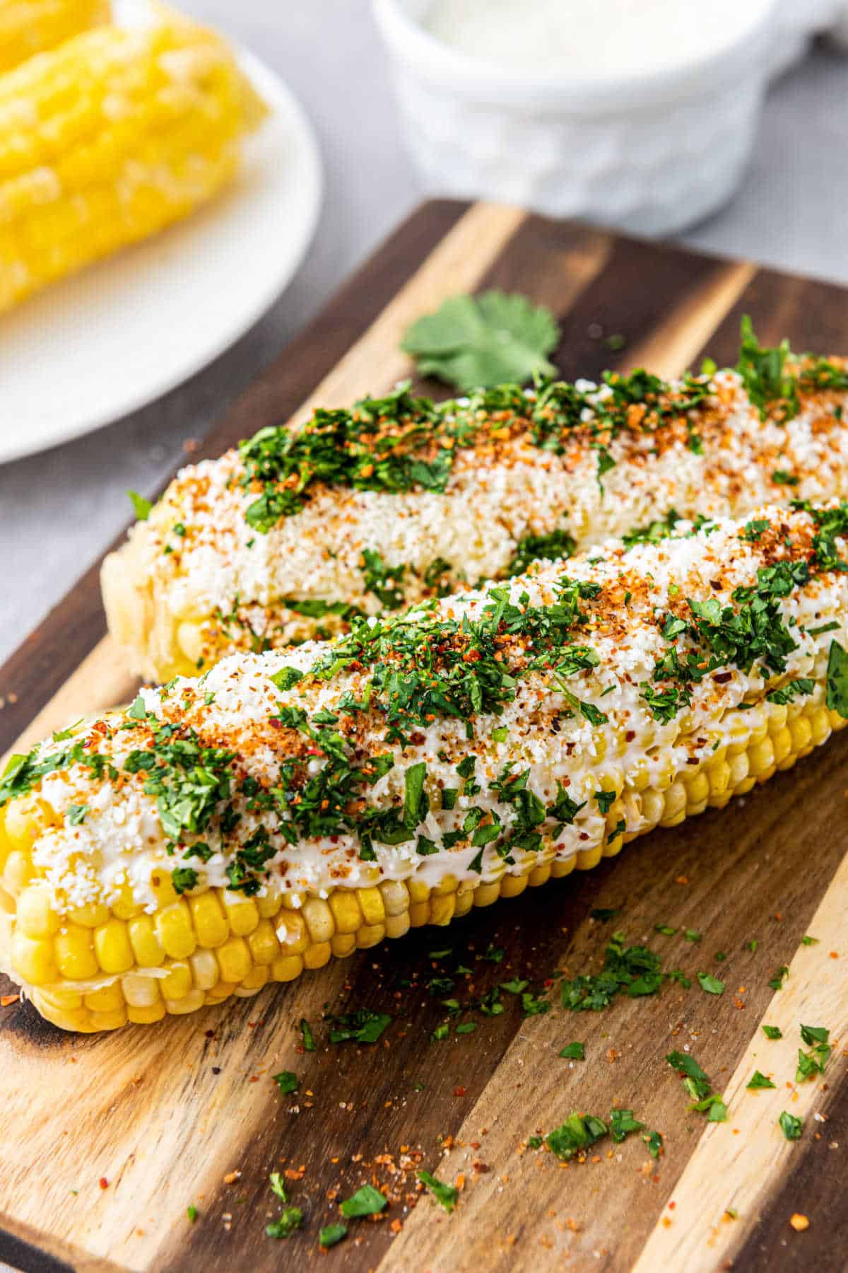 Two pieces of Elotes or Mexican Street Corn, on a wooden baord.