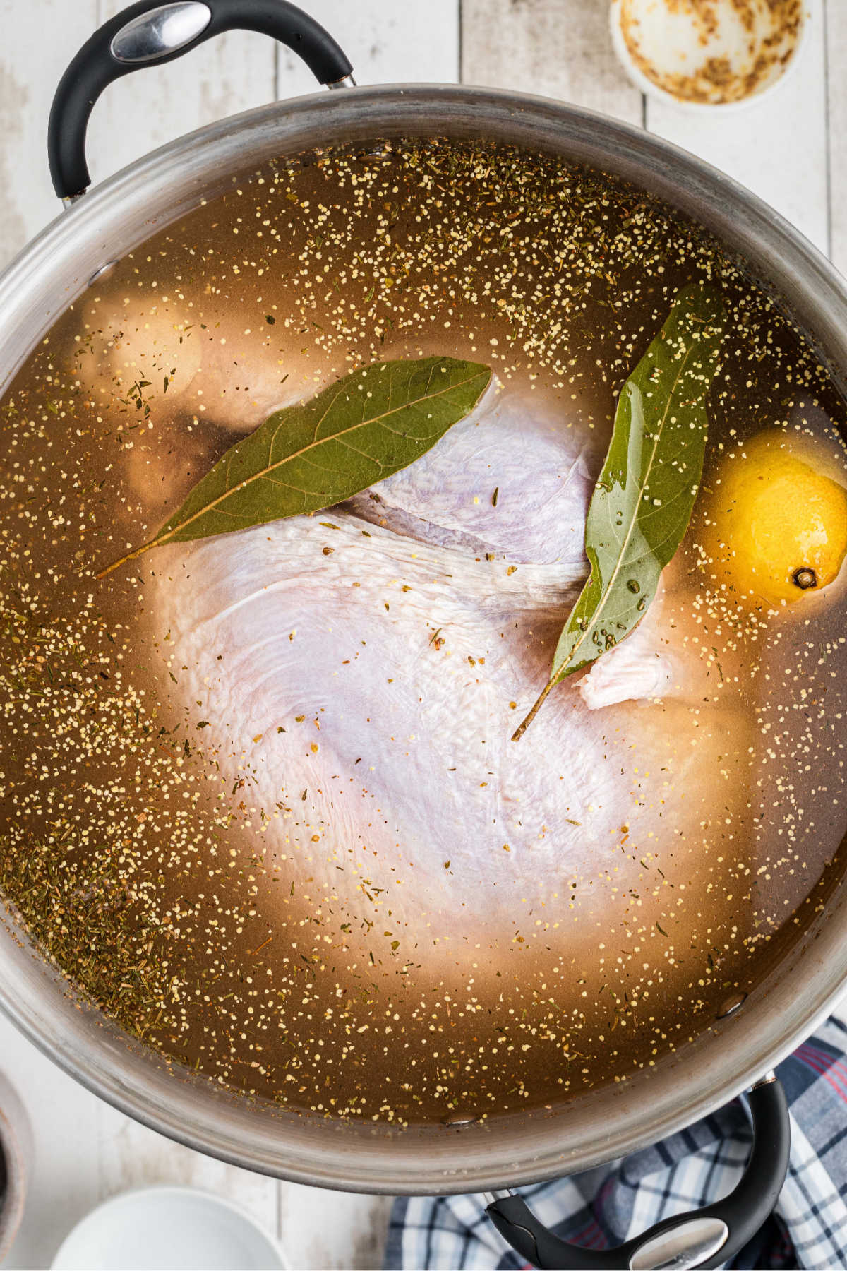 A large turkey sitting in a brine solution, with bay leaves, seasonings and lemon.
