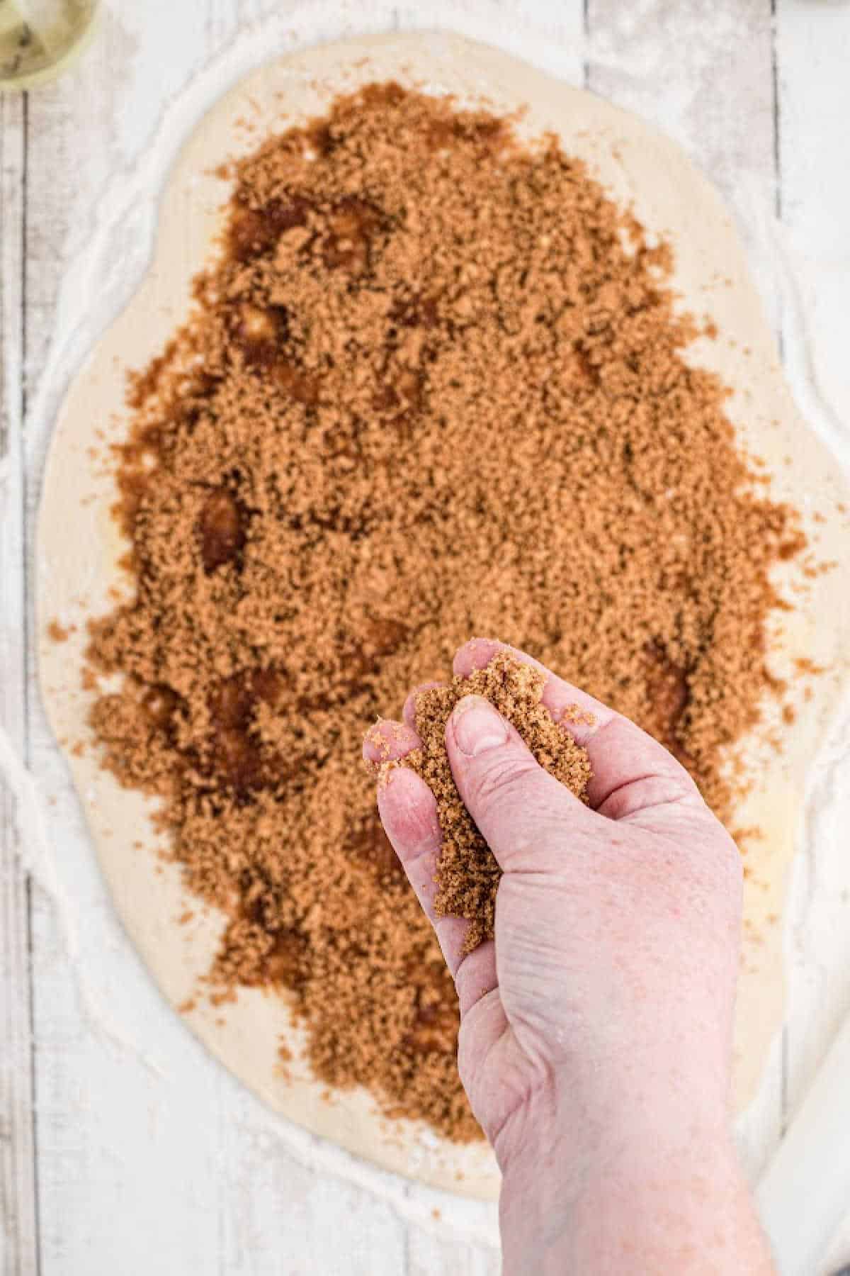 Brown sugar mixture being sprinkled onto a rolled out dough.