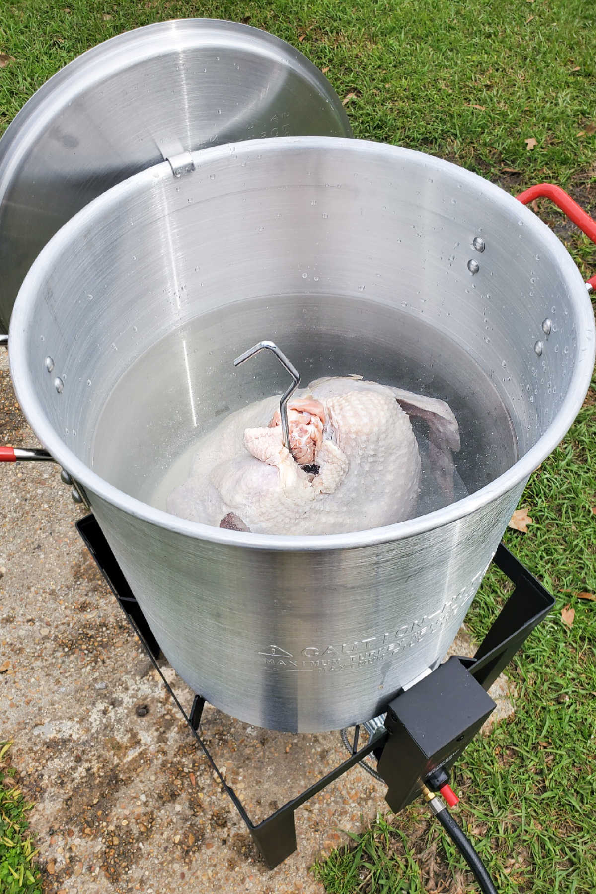 A large frying pot, with a turkey submerged in water.