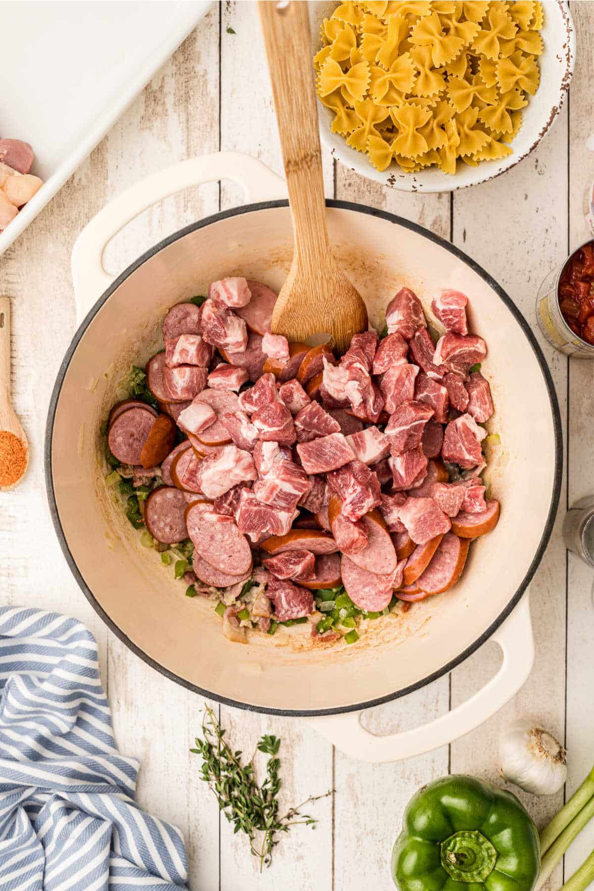 Chopped pork and sausage being added to a Dutch oven with other ingredients.