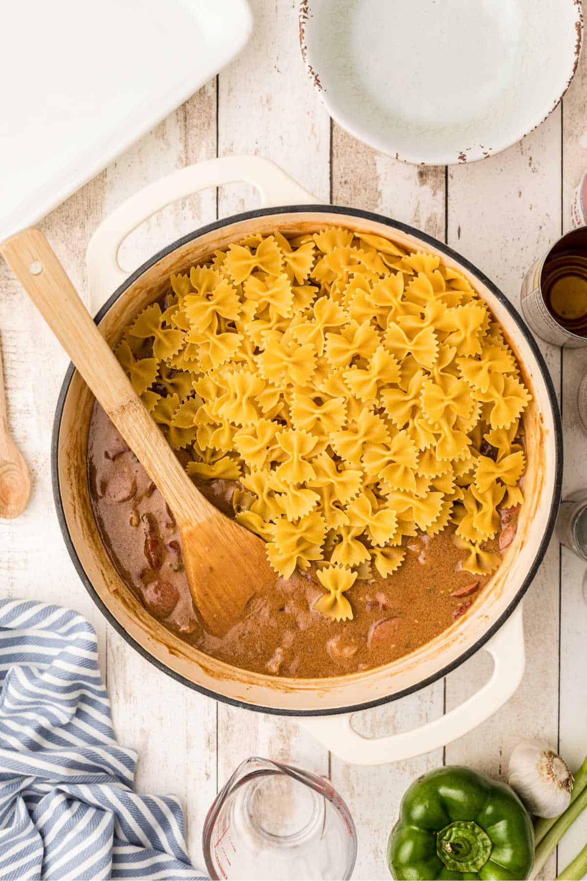 Pasta being added to a Dutch oven with Pastalaya ingredients.