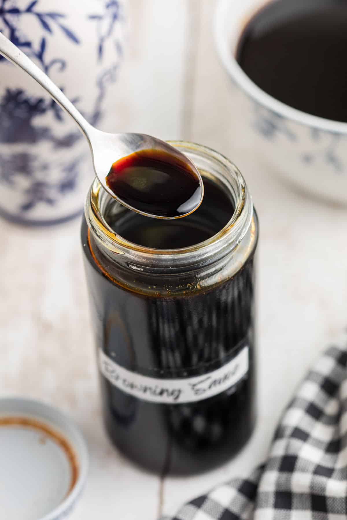 A jar of browning sauce, with a homemade label, with a spoon lifting some out.