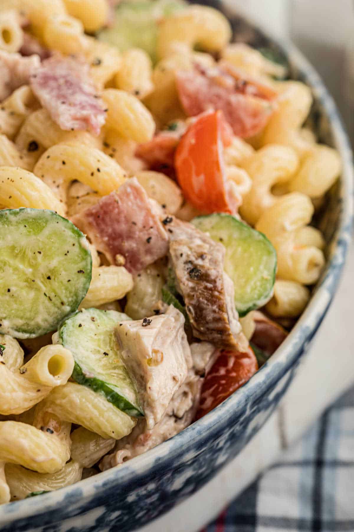 Super close up picture of a pasta salad, with chicken and bacon, in a blue bowl.