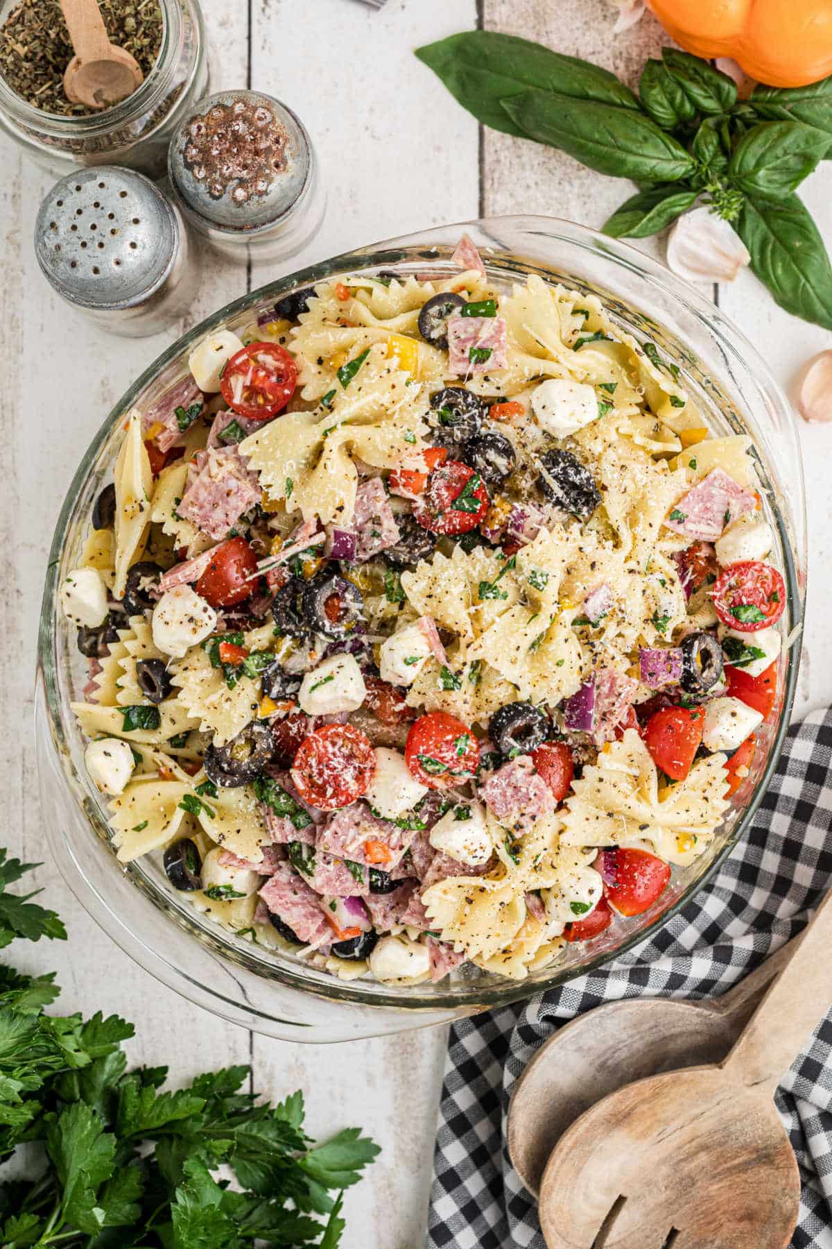 An overhead image of a bowl of Italian pasta salad, that has bowtie pasta, olives, feta cheese, tomatoes etc.
