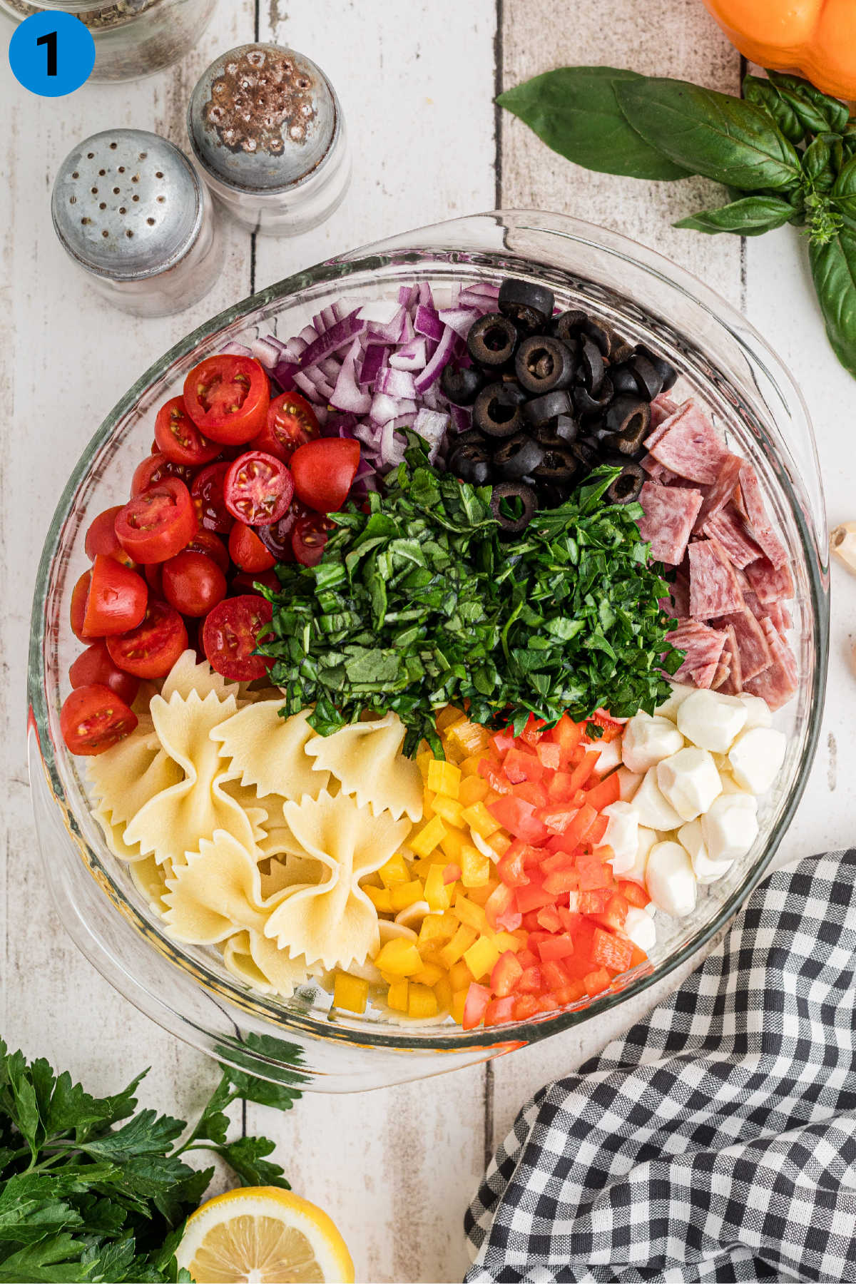 A large salad bowl filled with ingredients needed to make an Italian Pasta Salad.