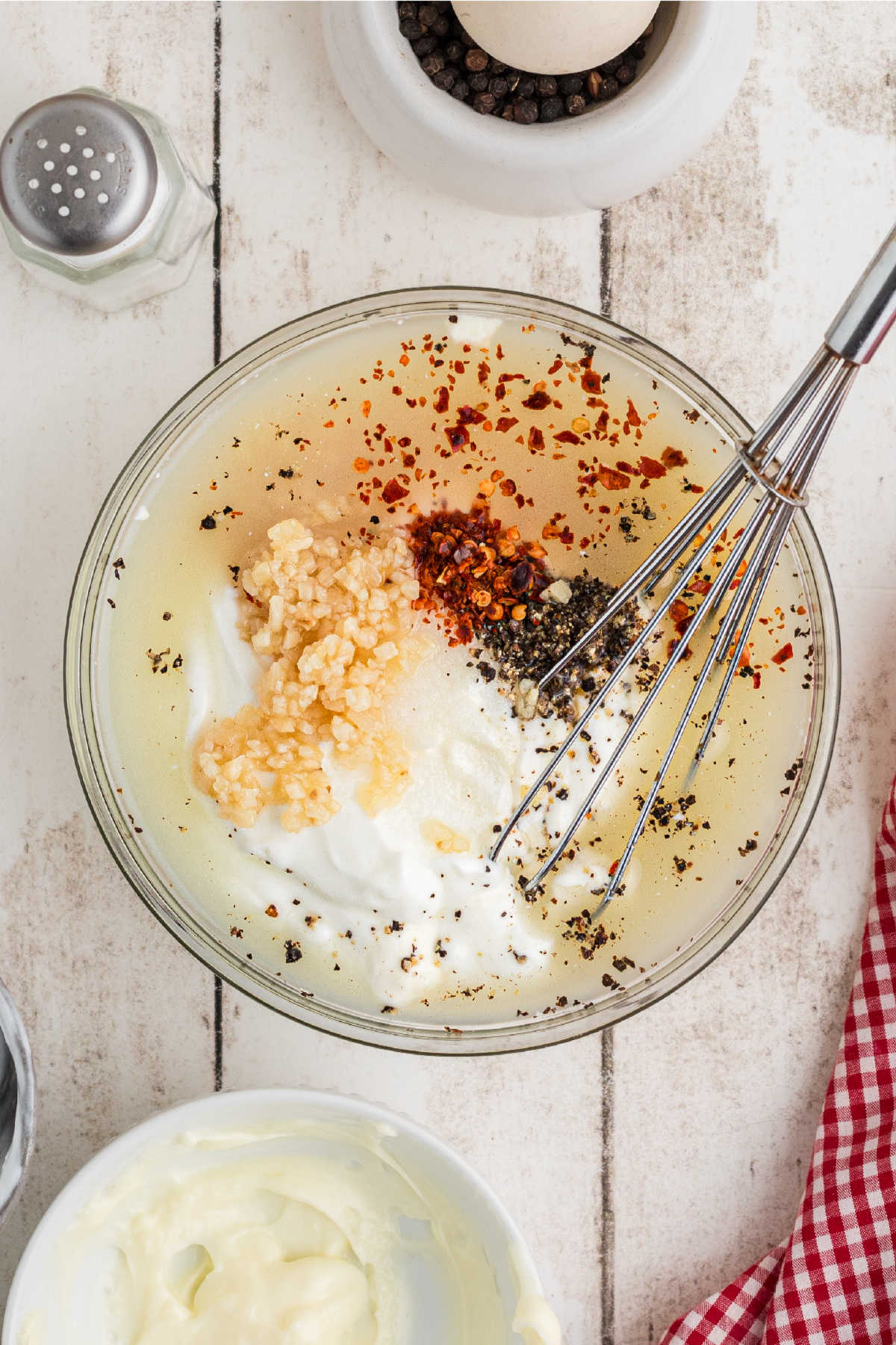 A smaller mixing bowl with salad dressing ingredients and a whisk.